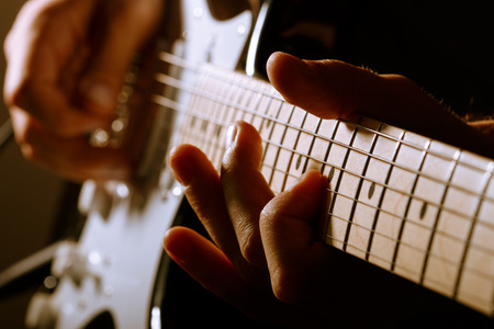 Hands of man playing electric guitar. Low key photo.