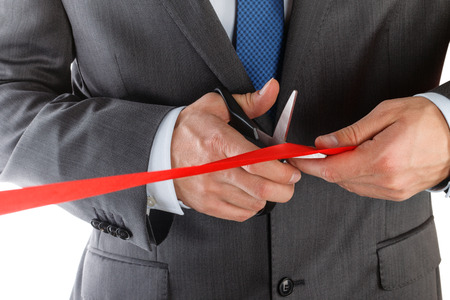Businessman in suit cutting red ribbon with pair of scissors isolated on white background. Grand opening concept. Traditional public festive ceremony.の写真素材