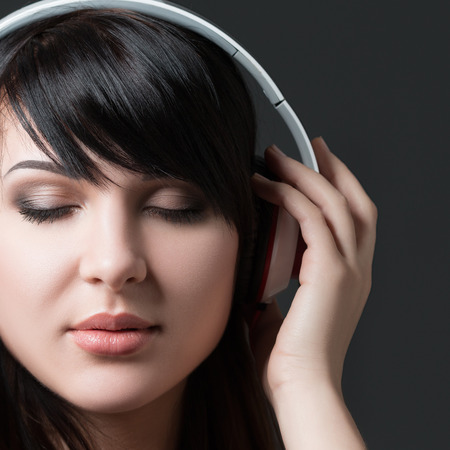 Close-up portrait of young beautiful brunette woman listening to music and holding white headphonesの写真素材