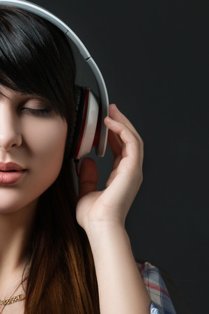Close-up portrait of young beautiful brunette woman listening to music with her eyes closed and holding white headphonesの写真素材