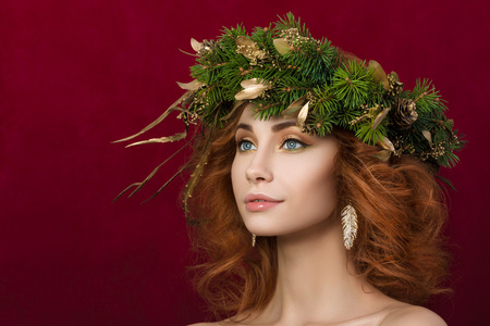 Portrait of young beautiful redhaired woman with firry wreath with golden leaves in her hair.の写真素材