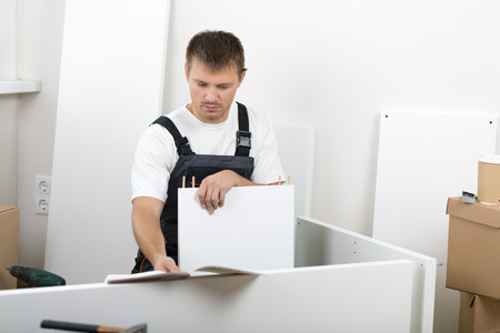 Frustrated man dressed in workers' overall reading instruction and putting together self assembly furniture. の写真素材
