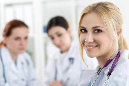 Portrait of smiling female medicine doctor with two colleagues working at background. Healthcare and medicine concept.の写真素材