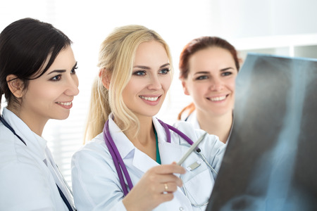 Three smiling female medicine doctor looking at x-ray picture. Healthcare and medicine concept.の写真素材