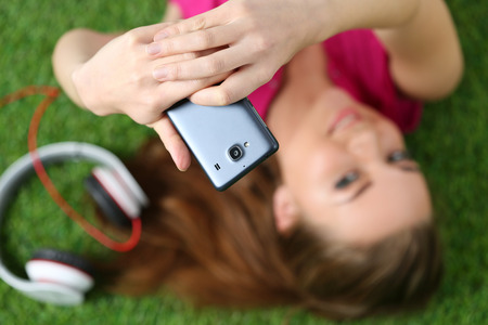 Young pretty girl taking self portrait with her smart phone laying on grass. Focus on phoneの写真素材