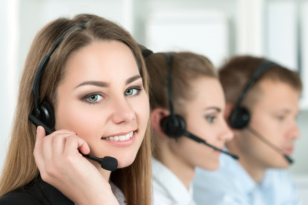 Portrait of call center worker accompanied by her team. Smiling customer support operator at work. Help and support conceptの写真素材