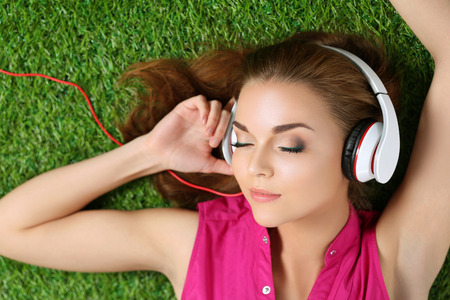 Young beautiful girl laying on the grass in park listening to music. Summertime and leisure concept. Top view. Copyspace.の写真素材