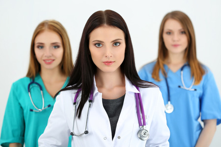 Portrait of young brunette female doctor surrounded by medical team, looking at camera. Healthcare and medicine concept.の写真素材