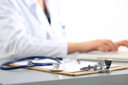 Medicine doctor's working place. Focus on stethoscope, doctor's hands typing something on background. Healthcare and medical concept. Copyspaceの写真素材