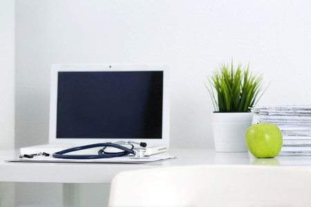 Medicine doctor's working table. Laptop, papers, green apple and stethoscope lying on table at physician's office. Healthcare and medical conceptの写真素材