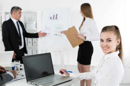 Business people meeting in office to discuss project. Young pretty female office worker looking at camera with her colleagues acting on background. Business meeting and teamwork conceptの写真素材