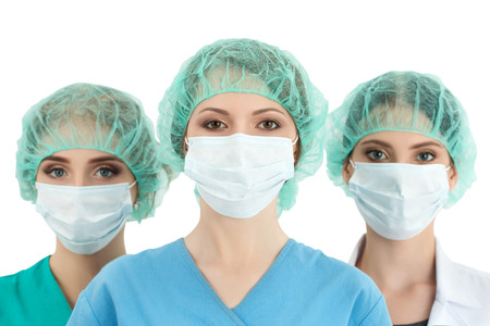 Young woman doctor in cap and face mask with two her collegues standing behind her. Healthcare, medical, surgery and team work conceptの写真素材