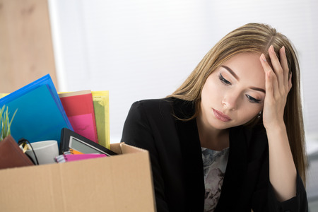 Young dismissed female worker in office sitting near carton box with her belongings. Getting fired concept.の写真素材
