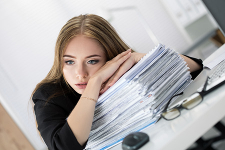 Tired business woman laying on heap of papers at her working place. Overwork, working overtime and...