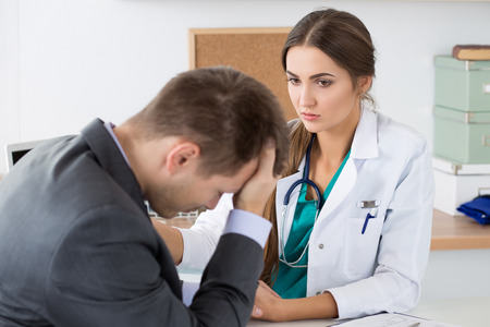 Friendly female medicine doctor's holding male patient's hand supporting him. Bad news, stress and depression concept.の写真素材
