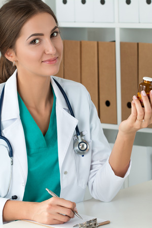 Smiling female medicine doctor holding bottle with pills and writing prescription. Healthcare, medical and pharmacy concept.の写真素材