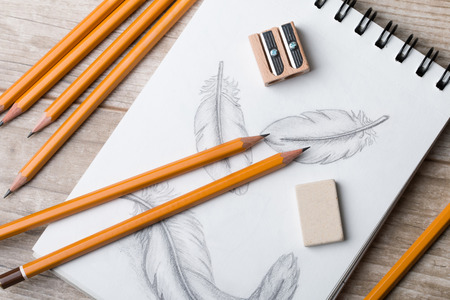 Close-up view of artist's or designer's table. Pencils, sharpner and eraser laying on sketch book...
