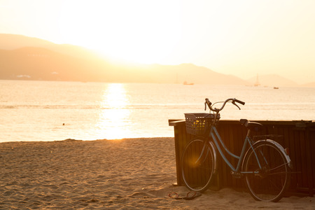 Blue bicycle standing on sandy beach during sunrise. Freedom and happiness concept. Old fashioned sepia colors. Post card view.の写真素材