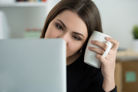 Tired female employee at workplace in office holding cup of tea. Sleepy worker early in the morning after late night work. Overworking, making mistake, stress, termination or depression conceptの写真素材