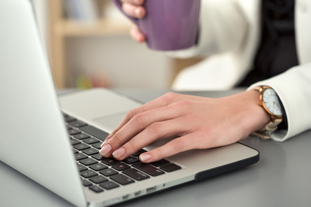 Close up view of female student at workplace holding cup of tea and working at laptop. Woman writing letter, list, plan, making notes, doing homework. Business, education, self development conceptの写真素材
