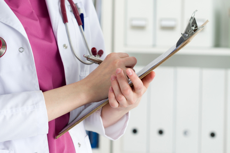 Close up view of female doctor hands holding clipping pad and writing patient history or prescribing some medicines. Healthcare and medical concept.の写真素材