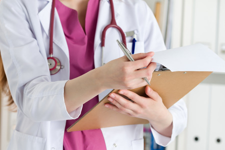 Close up view of female doctor hands holding clipping pad and reading patient history or prescribing some medicines. Healthcare and medical concept.の写真素材