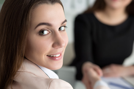 Two women handshake in office. Businesswomen shaking hands. Lady looks back over her shoulder. Partnership, business and collaboration concept. Partners made deal. Formal greeting gestureの写真素材