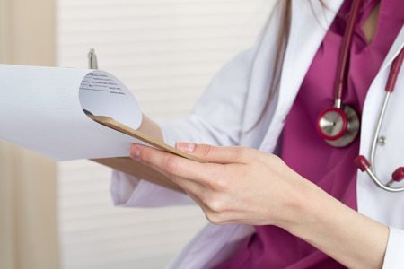 Close up view of female doctor hands holding clipping pad and filling patient history or prescribing some medicines. Healthcare and medical concept.の写真素材
