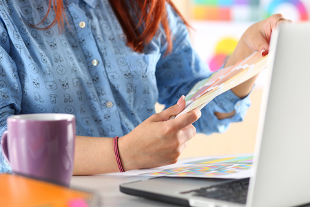 Hands of female designer in office working with colour samples. Woman at workplace choosing...