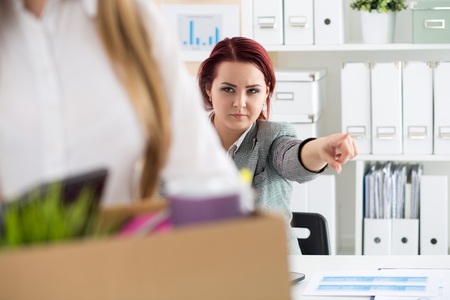 Boss dismissing an employee. Dejected fired office worker carrying a box full of belongings. Getting fired concept.の写真素材