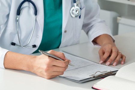 Close up view of female medicine doctors hands filling patient medical form. Physician working with paper in hospital office room. Therapeutist sitting at working table making some paperworkの写真素材
