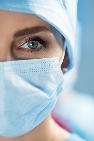 Close up portrait of adult female surgeon doctor wearing protective mask and cap. Half face closeup. Healthcare, medical education, emergency medical service and surgery conceptの写真素材
