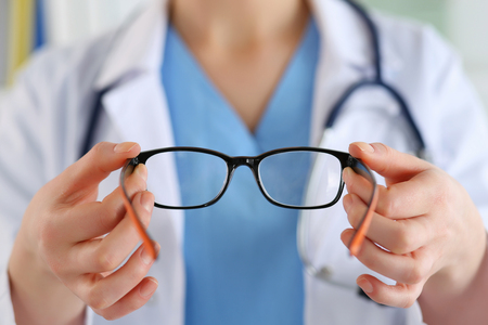 Female oculist doctor hands giving pair of black glasses to patient. Eyesight correction. Ophthalmology, excellent vision or optician shop concept. Laser surgery alternative.の写真素材