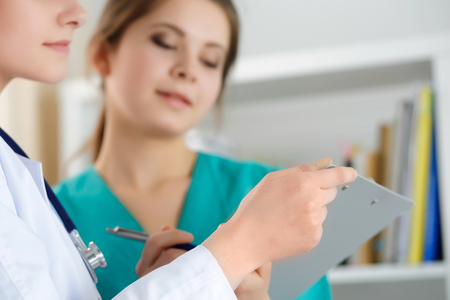 Two female medicine doctors working at their office discussing diagnose and filling patient registration or medical history form. Hands closeup Medical service, education, therapy and healthcare conceptの写真素材