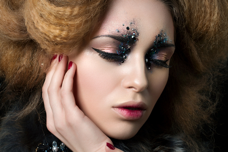 Beauty portrait of young woman with fashion makeup with rhinestones touching her face. Studio shot. Carnival or party makeupの写真素材