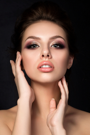Portrait of young beautiful woman with evening make up touching her face over black background. Red and gold multicolored smokey eyes. Luxury skincare and modern fashion makeup concept. Studio shot.の写真素材