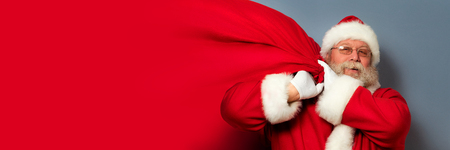 Santa Claus is holding a huge bag of gifts on his shoulder. Copyspace. Christmas miracle, celebration and gifts concept.の写真素材