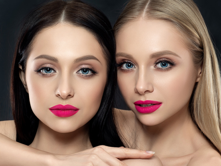 Closeup portrait of two young beautiful women over black background. Bright pink lipstick. Skin care, cosmetics, SPA therapy or cosmetology conceptの写真素材