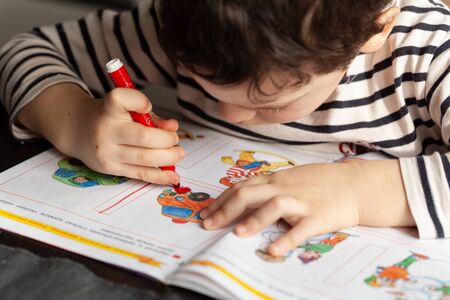 Small boy at home drawing lines in book hometask