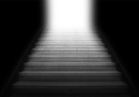Staircase going up to the white light from the dark area,gray color monotoneの写真素材