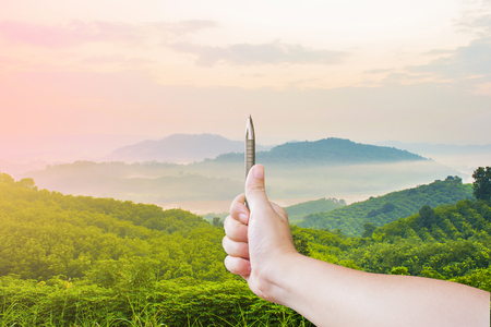 A hands are holding pen perpendicular to the nature to measure with the mountain and sky backgroundの写真素材