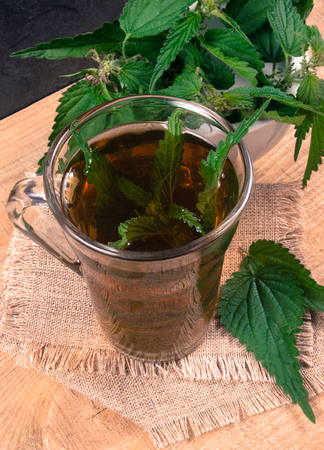Healing tea with nettle. Tea in a glass cup on a wooden table. Concept of herbal medicine.の写真素材