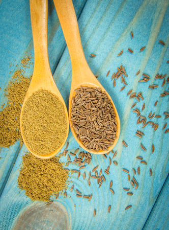 Close up on ground cumin in a spoon and whole cumin. Blue wooden background.の写真素材