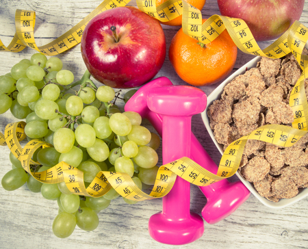 Dumbbells, measuring tape, flakes and fresh fruits on wooden table. Healthy eating concept. Diet.の写真素材