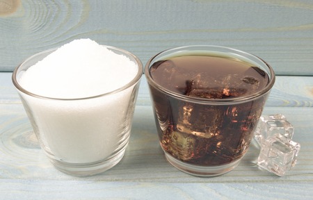 Carbonated drink with ice on a blue background. The concept of sugar content in sweetened beverages....