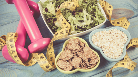 Healthy eating, dieting, slimming and weigh loss concept -dumbeells, measuring tape and salad.の写真素材