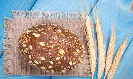 Multi-grain bread rolls and cereal ears on on blue wooden table. Healthy diet.