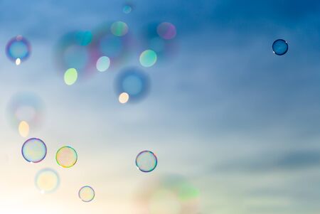 Colorful soap bubbles flying in a blue and orange sky while the sun is setting.の写真素材