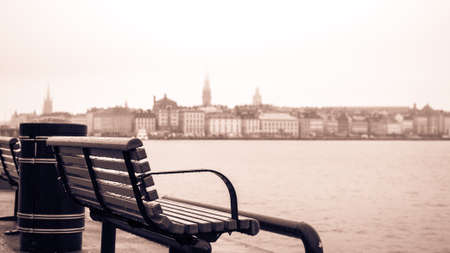 Lonely bench on pier with scenic panorama of misty, rainy Stockholm in the background. Toned imageの写真素材