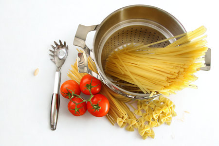 A still life arrangement of uncooked pasta, cherry tomatoes, and a pasta server, suggesting preparation for a meal.の写真素材